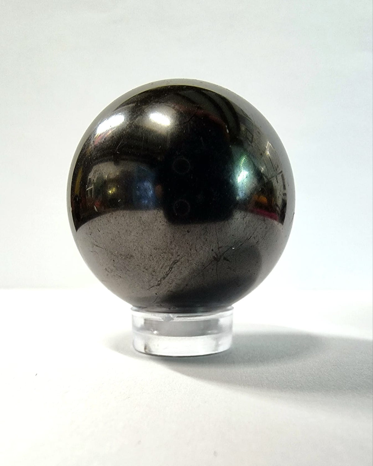 A polished shungite sphere with clear acrylic stand great for absorbing electromagnetic smog.