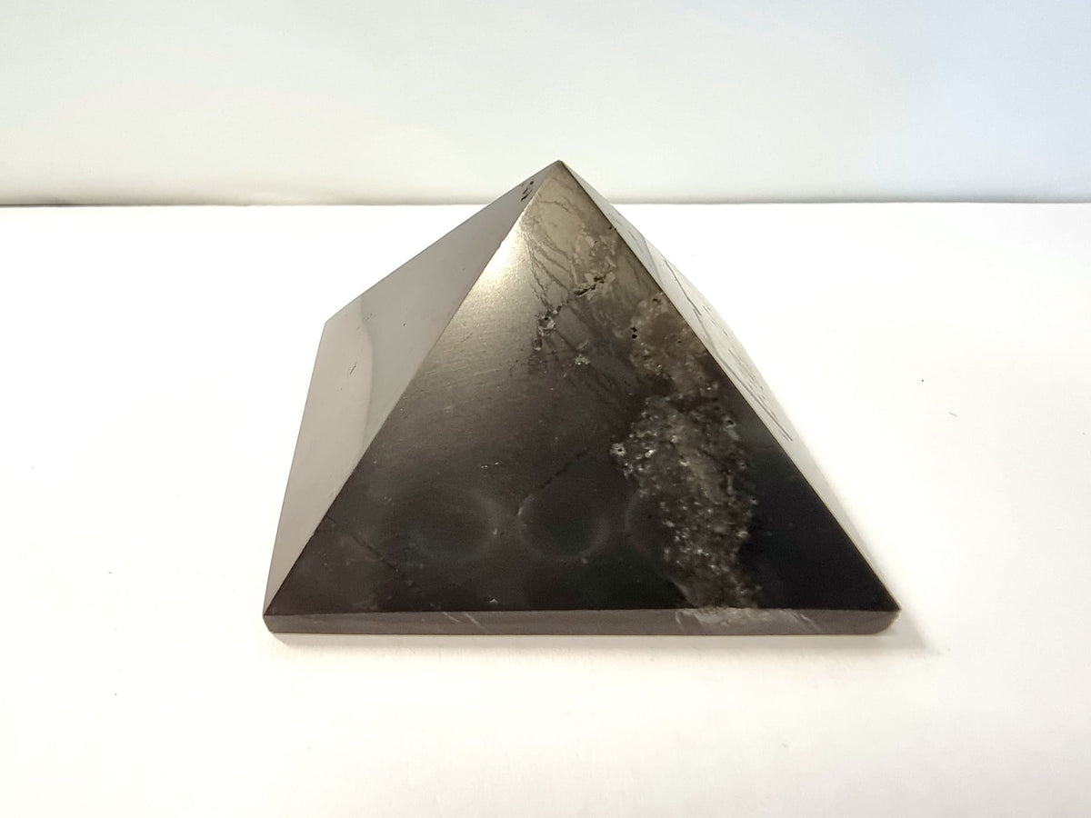 A polished black shungite crystal pyramid providing protection on your spiritual journey.