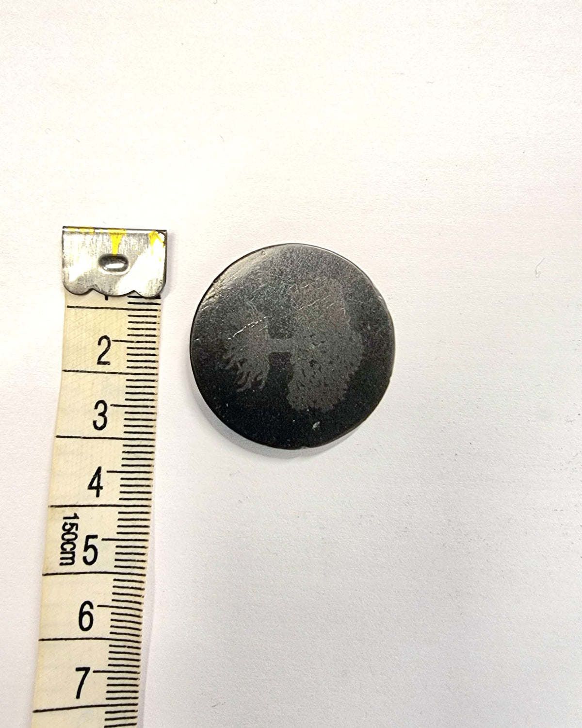 A sticker made from black shungite with a Tree of Life symbol etched into it.  Used to attach to electronic devices to absorb EMF.