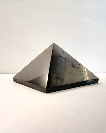 A polished black shungite crystal pyramid providing protection on your spiritual journey.